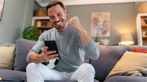 Egy fiatalember kezében okostelefonnal, rajta sportfogadási alkalmazással